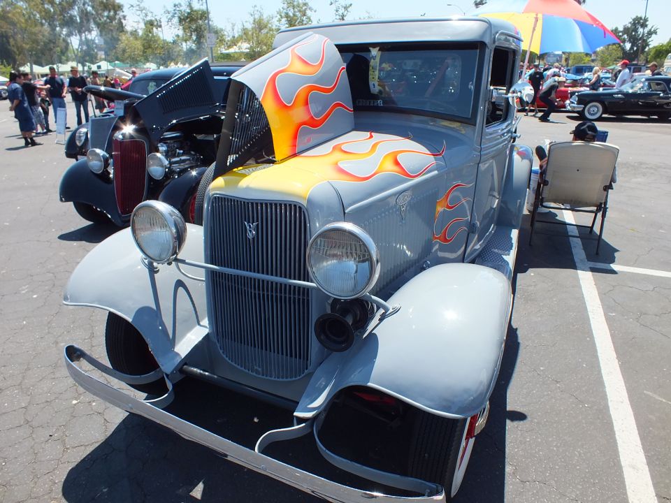 Gray 1932 Ford coupe hot rod with orange flame paint and open hood at car show