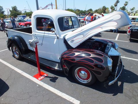 White and black flamed pickup hot rod with open hood and Coca-Cola jack stand at car show