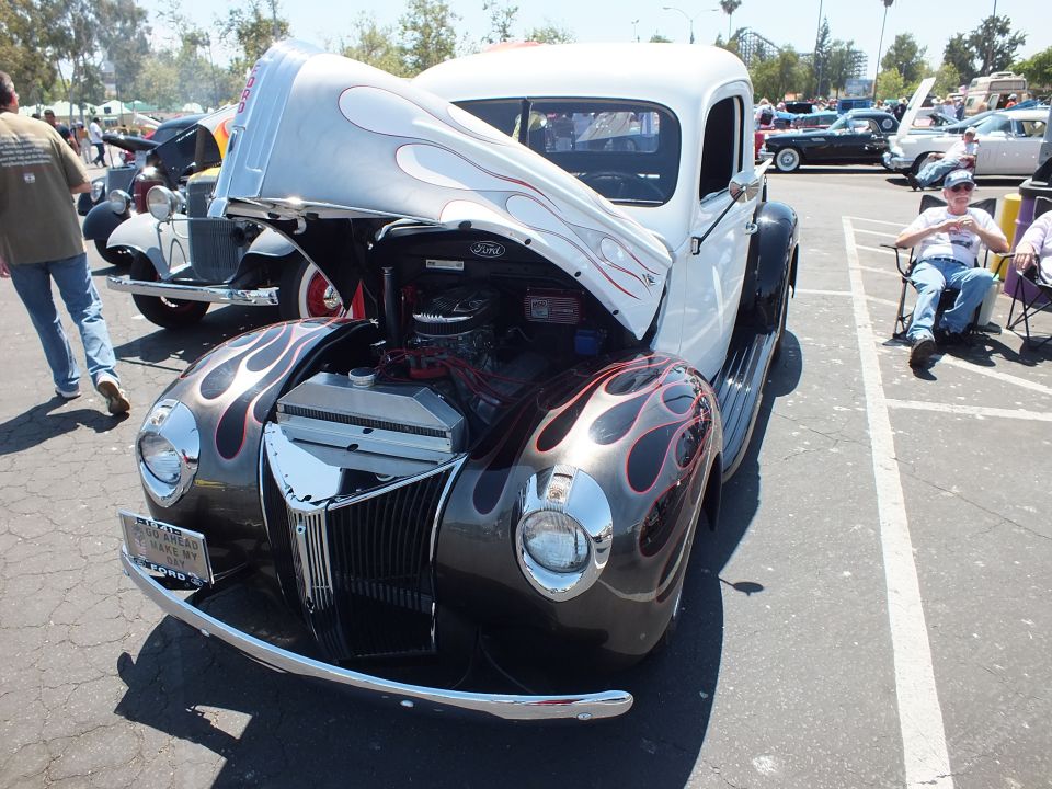 White and black flamed Ford coupe hot rod with open hood and Ford grille at car show