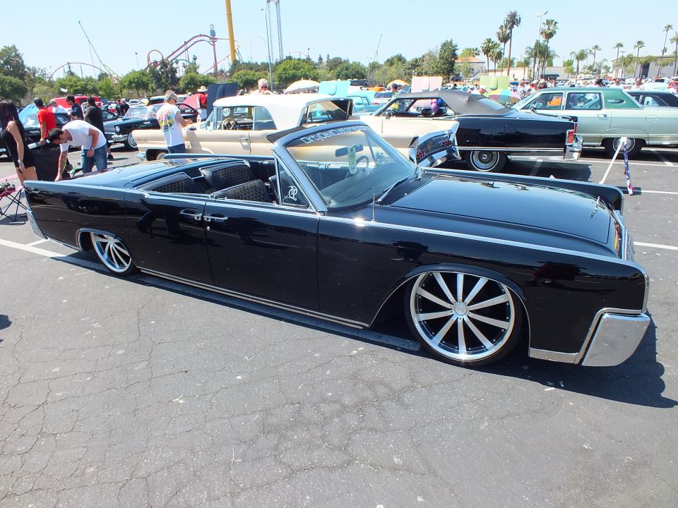 Lowered black 1960s Lincoln Continental convertible with chrome wheels at outdoor car show