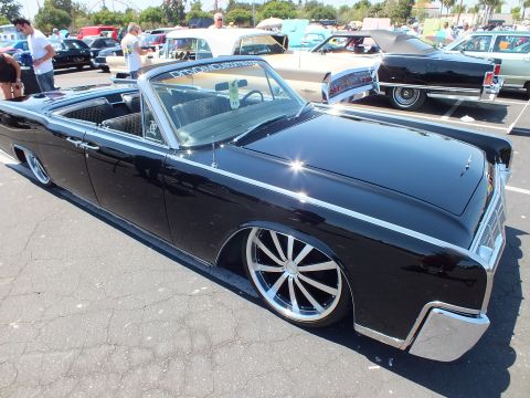 Black 1960s Lincoln Continental convertible lowered on chrome wheels, side view at car show