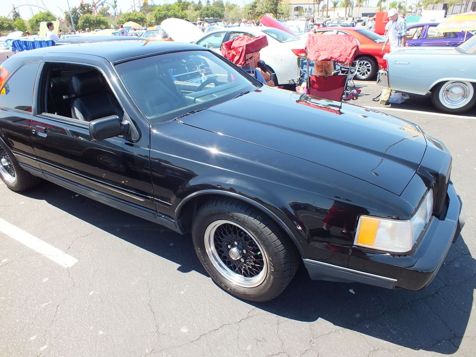 Black 1980s Lincoln Mark VII coupe with composite headlights at car show