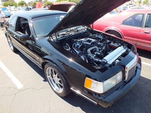 Black Lincoln Mark VII coupe with open hood showing modified engine at car show