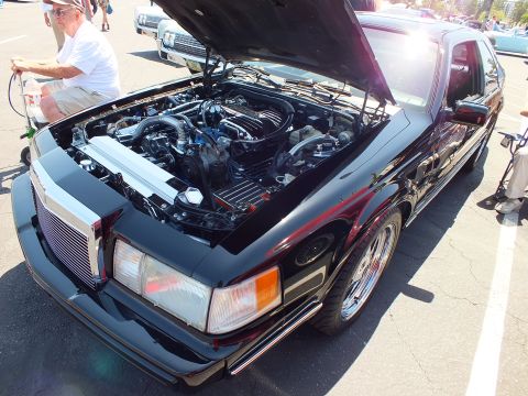 Black Lincoln Mark VII coupe with open hood and detailed engine bay at car show