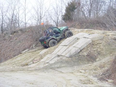 1992 Ford Bronco - An off-road vehicle navigates a challenging rocky terrain with an orange flag on top.