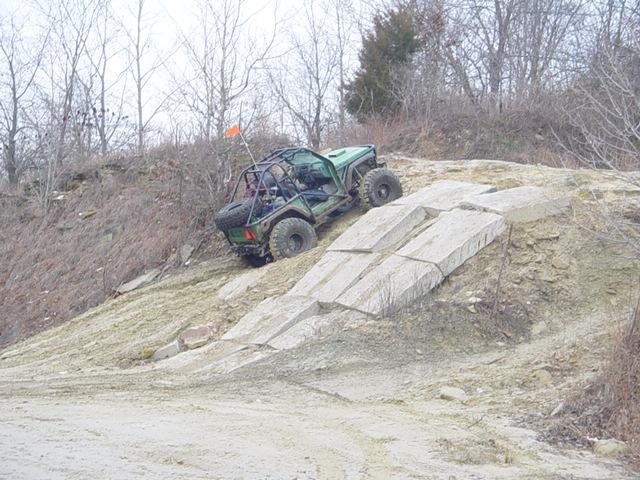 Green off-road vehicle with roll cage climbing a rocky incline