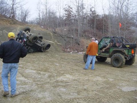 1992 Ford Bronco - Two off-road vehicles are in a muddy area, with one vehicle flipped on its side on a slope.