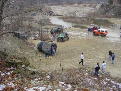 1992 Ford Bronco - Off-road vehicles navigate a challenging muddy terrain with onlookers present.