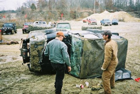 1992 Ford Bronco - Two men observe a mud-covered, overturned SUV at an outdoor event.