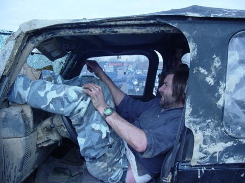 1992 Ford Bronco - Man sits in the driver's seat of a muddy vehicle, with another vehicle in the background.