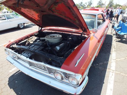 Copper-orange classic car with hood up exposing V8 engine at show