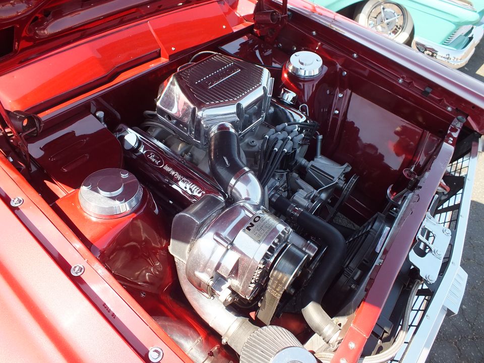 Chromed supercharged V8 engine in red car engine bay at car show