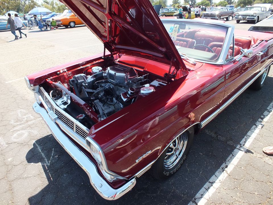 Dark red convertible classic car with hood up showing engine at outdoor car show