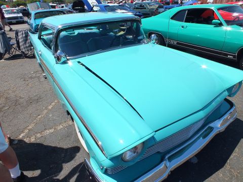 Turquoise classic hardtop car parked at car show with green muscle car behind