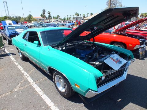 Teal Ford Torino fastback with open hood at outdoor car show