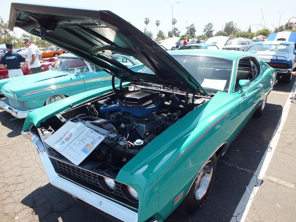 Teal Ford Torino fastback with open hood and engine display at car show