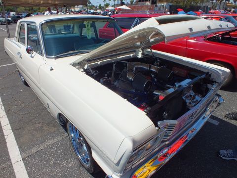 White classic sedan with open hood showing engine at outdoor car show