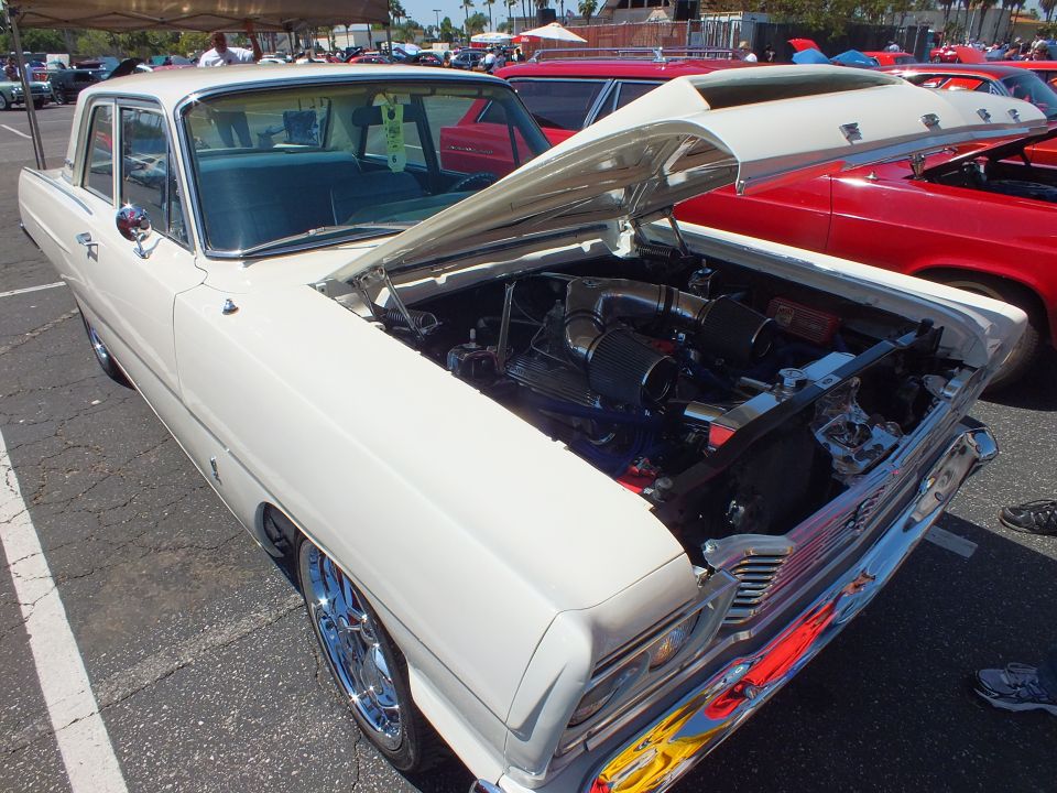 White classic sedan with open hood showing engine at outdoor car show