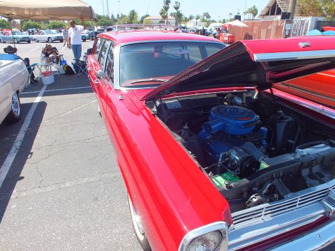 Red classic Ford sedan with open hood showing blue engine at car show
