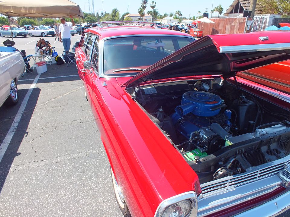 Red classic Ford sedan with open hood showing blue engine at car show