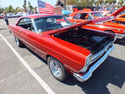 Red Ford Fairlane hardtop with open hood and American flag at car show
