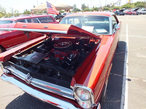 Copper-red Ford hardtop with open hood and American flag at car show
