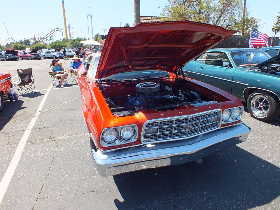 Orange Ford Torino with open hood and FORD grille lettering at car show