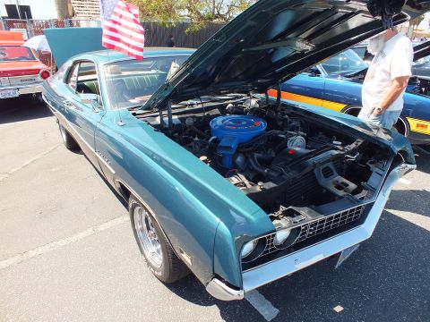 Teal Ford Torino fastback with open hood and blue engine at car show