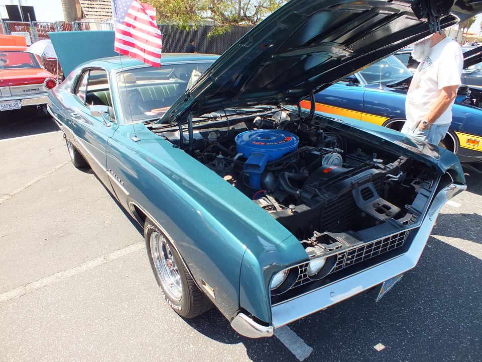 Teal Ford Torino fastback with open hood and blue engine at car show