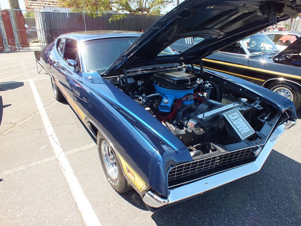 Dark blue muscle car with gold lower stripe and open hood showing V8 engine