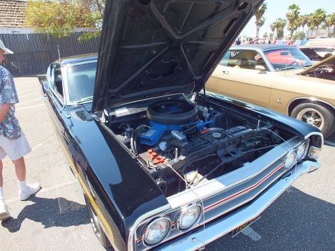 Black muscle car with red stripe and open hood showing V8 engine at car show