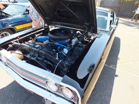 Black classic car front quarter with open hood and blue V8 engine, red stripe trim