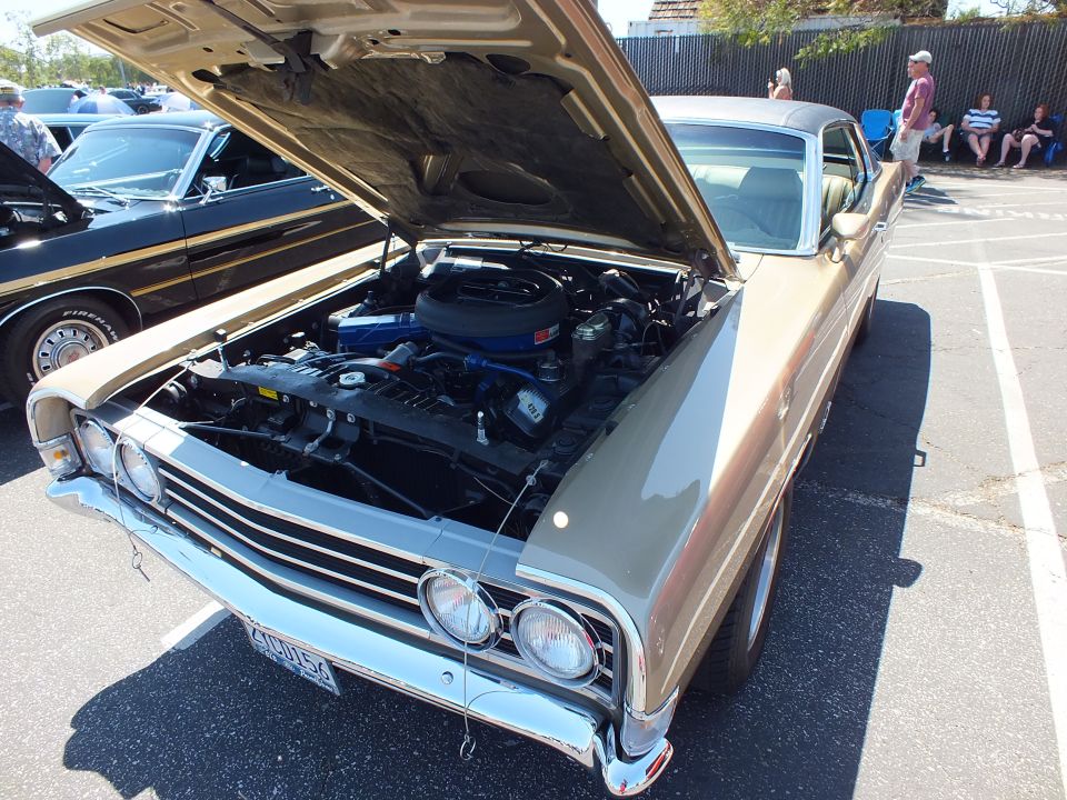Gold classic car front with hood up showing black air cleaner and blue valve covers