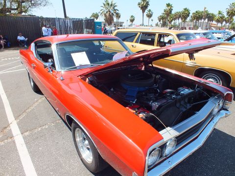 Orange-red fastback muscle car with open hood and V8 engine at car show