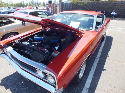 Orange-red classic muscle car front quarter with open hood and blue V8 engine