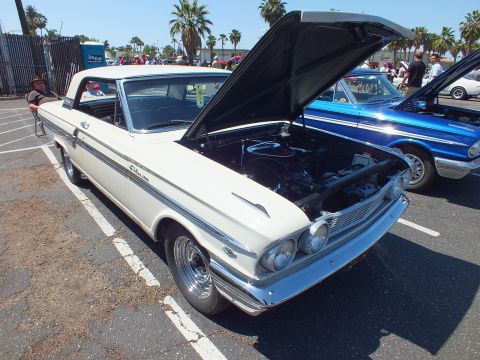 White two-door hardtop with open hood and side script badging at car show