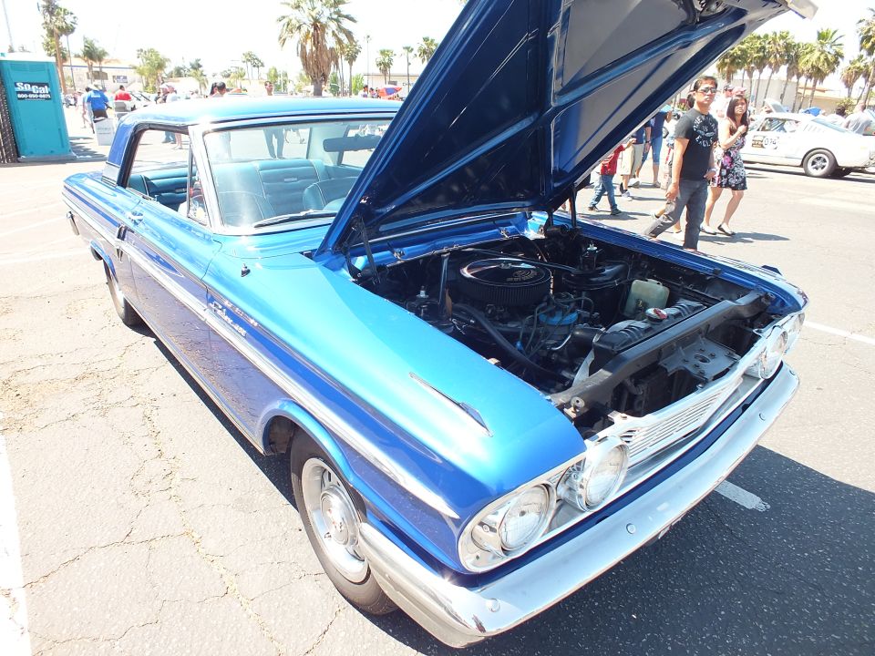 Blue two-door hardtop with hood scoop and open hood showing engine at car show