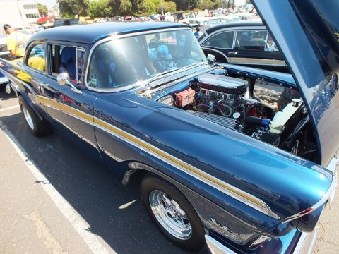 Dark blue 1950s sedan with gold stripe, open hood and chrome V8 engine