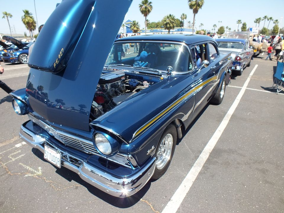 Dark blue 1950s sedan with gold stripe, open hood and chrome wheels at car show