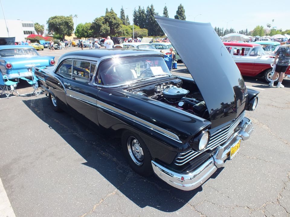 Black 1950s two-door sedan with chrome trim and open hood at outdoor car show