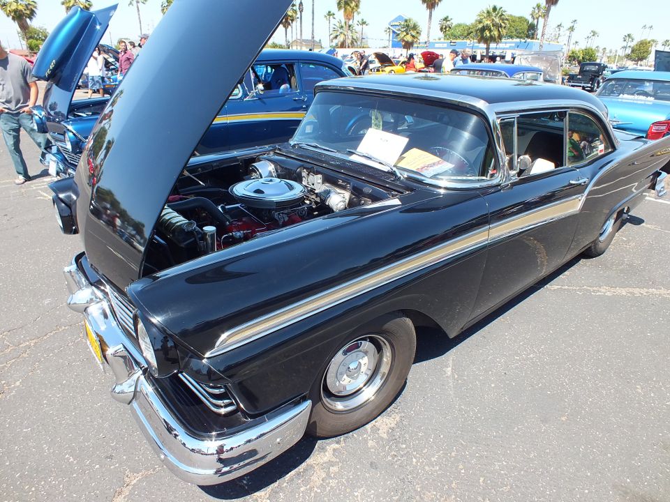 Black 1950s two-door hardtop with gold stripe and open hood showing engine
