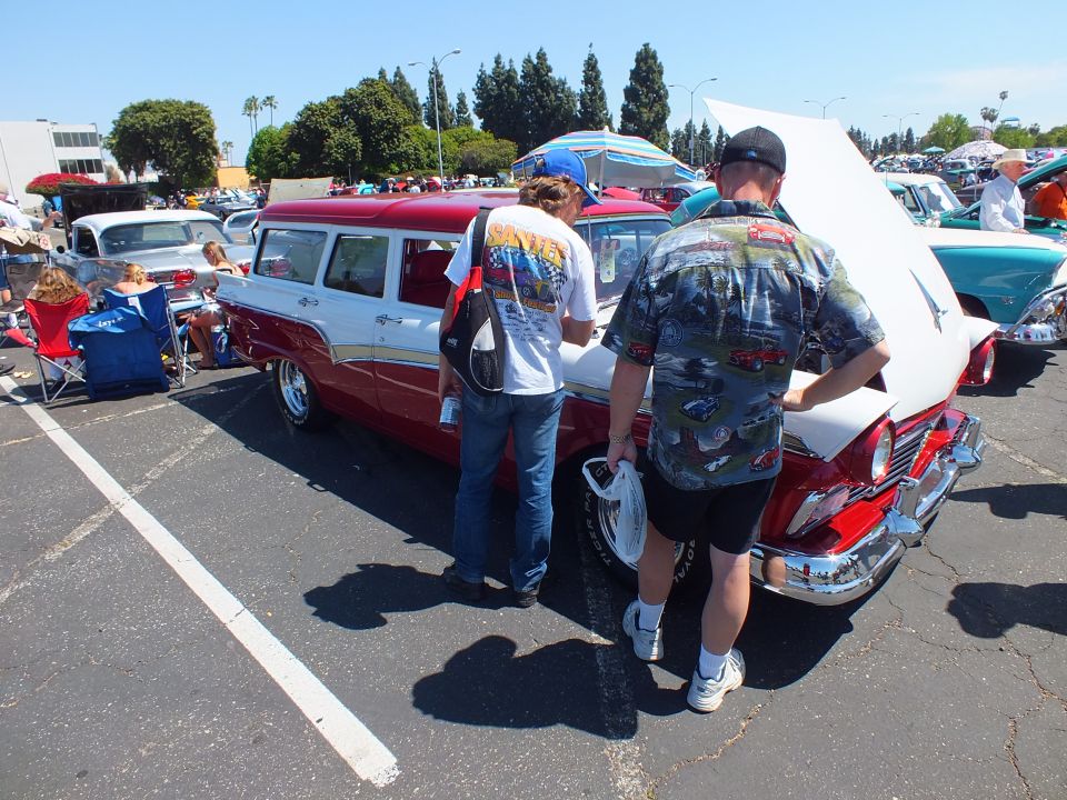 Red and white 1950s station wagon with two men in patterned shirts looking at it