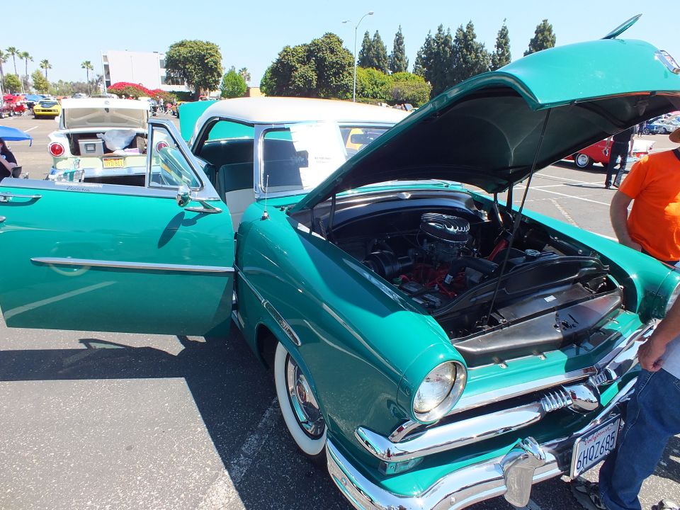 Teal 1950s Ford convertible with open hood and door at outdoor car show