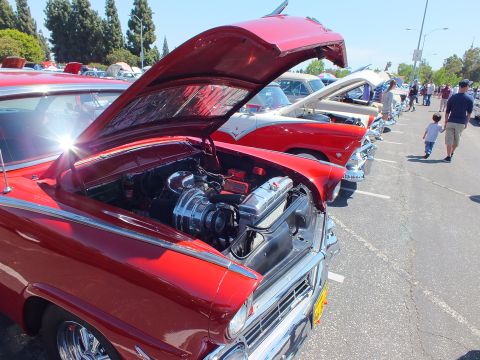 Dark red 1950s car with open hood showing chrome engine in row at car show