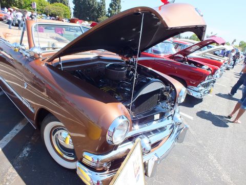 Brown 1950s car with open hood beside other classics at car show