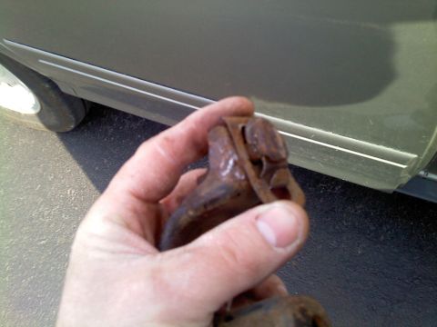 1999 Mercury Grand Marquis - Close-up of a rusty metal part, with a car's side and tire visible in the background.
