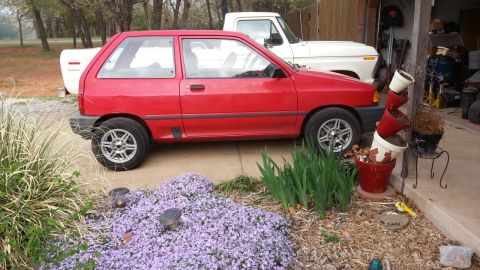 1991 Ford Festiva - A red 1991 Ford Festiva is parked beside a white pickup truck in a driveway.