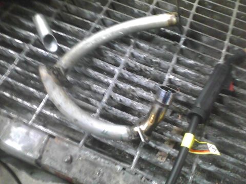 2003 Ford Crown Victoria - A section of exhaust pipe rests on a metal grate, with a welding tool visible to the right.