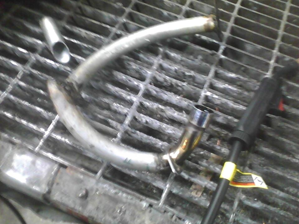 Curved metal exhaust pipe section on a metal grate, with a welding tool nearby
