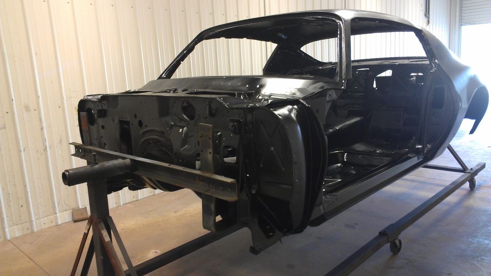 Car body shell on a stand, undergoing restoration. Body lines suggest a 1970s muscle car
